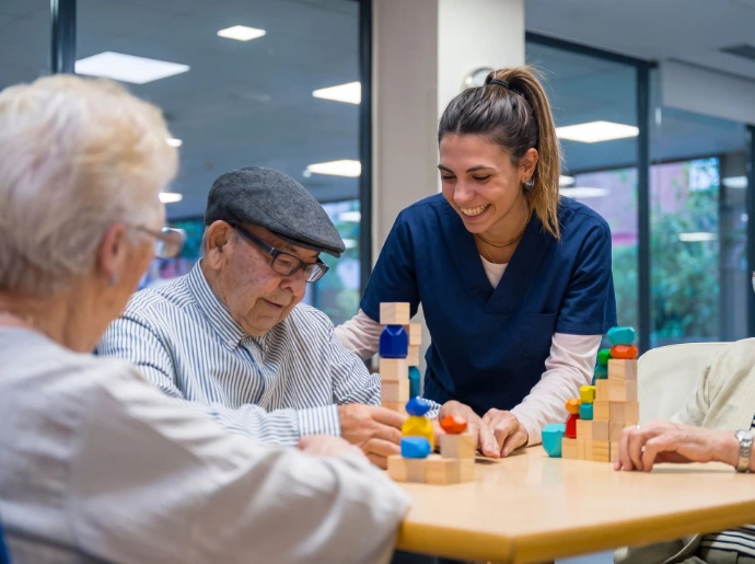 La acompañante juega con bloques de madera junto a los clientes mayores durante una actividad de ocupación.